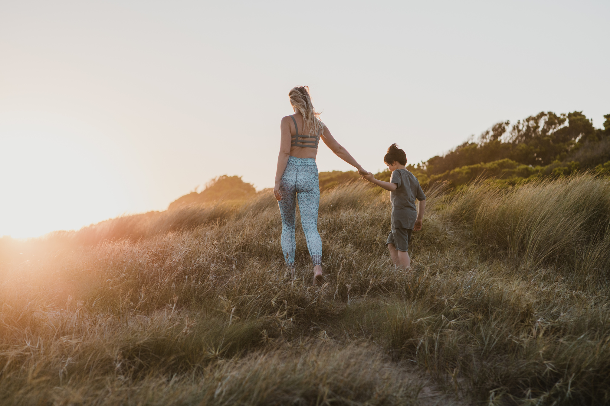 Jacintha and her son walking hand in hand through tall grass at sunset
