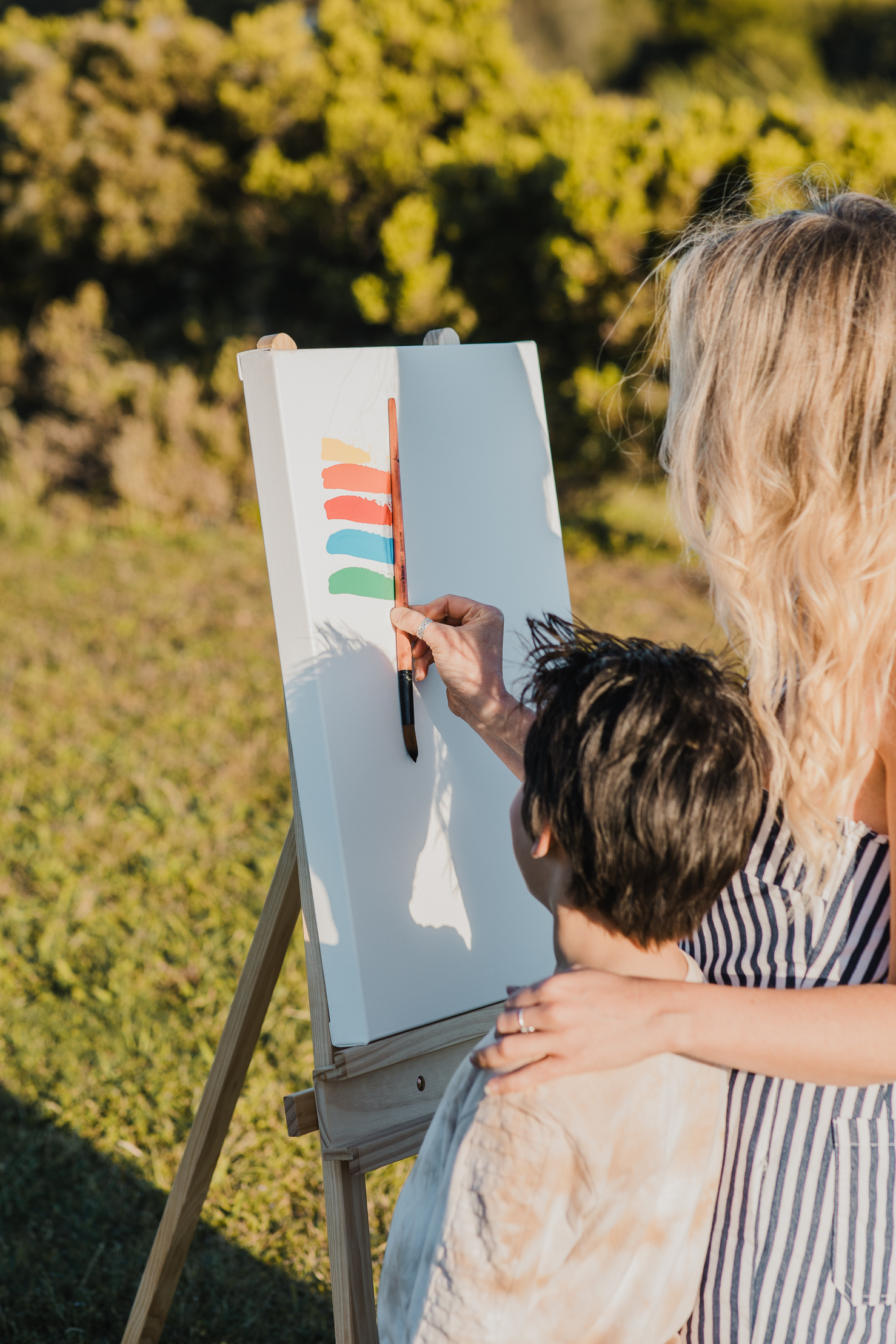 Jacintha painting on a canvas outdoors with her son